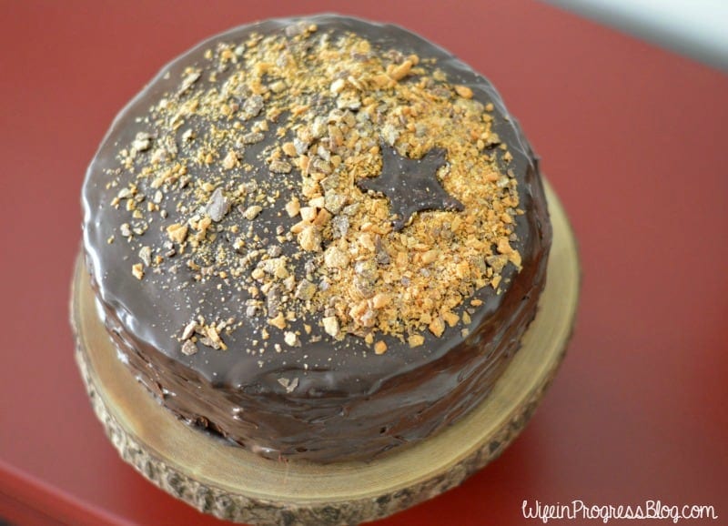A close up of the top of a chocolate-frosted cake with crunchy bits on top