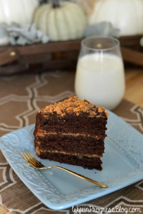 A large slice of chocolate cake, resting on a decorative, light blue plate with a glass of milk nearby