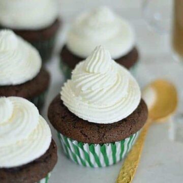 Brown cupcakes in a green and white striped cupcake wrapper, topped with peaks of white frosting