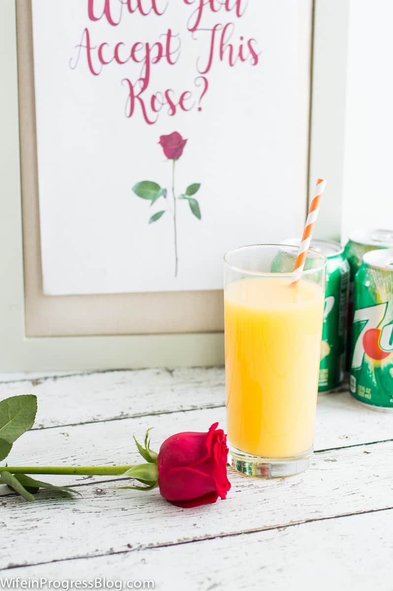 A glass of juice and cans of 7UP soda in the background, along with a rose and a frame that reads \"Will you accept this rose?\"