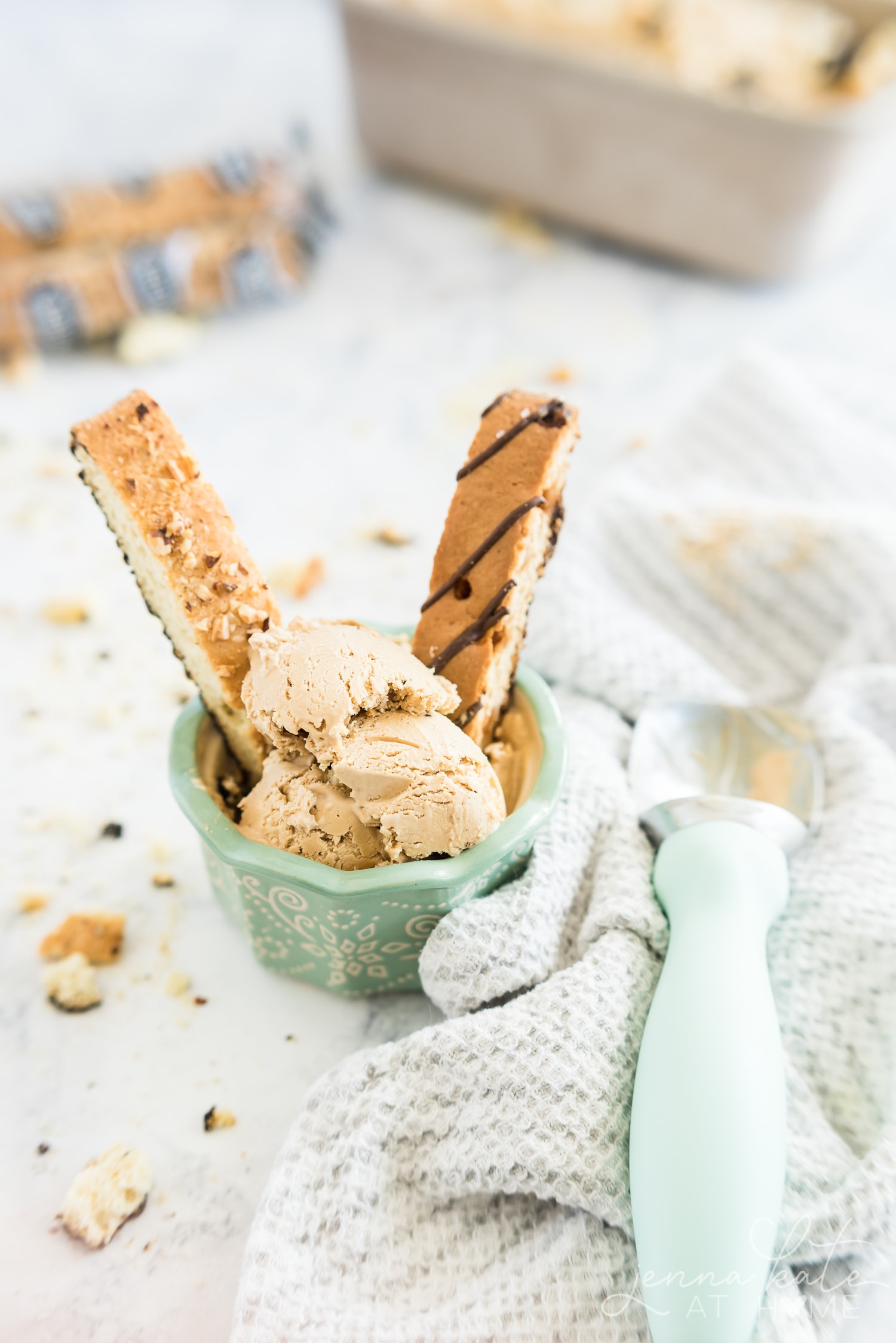 Scoops of ice cream in a small bowl with two biscotti in it