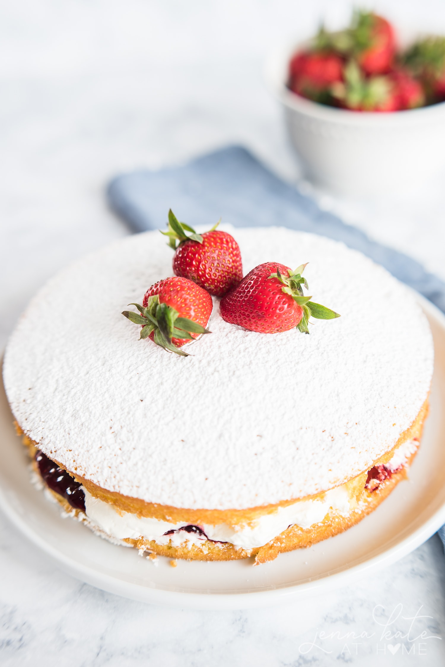 Top of victoria sponge cake, dusted with powdered sugar and topped with fresh whole strawberries