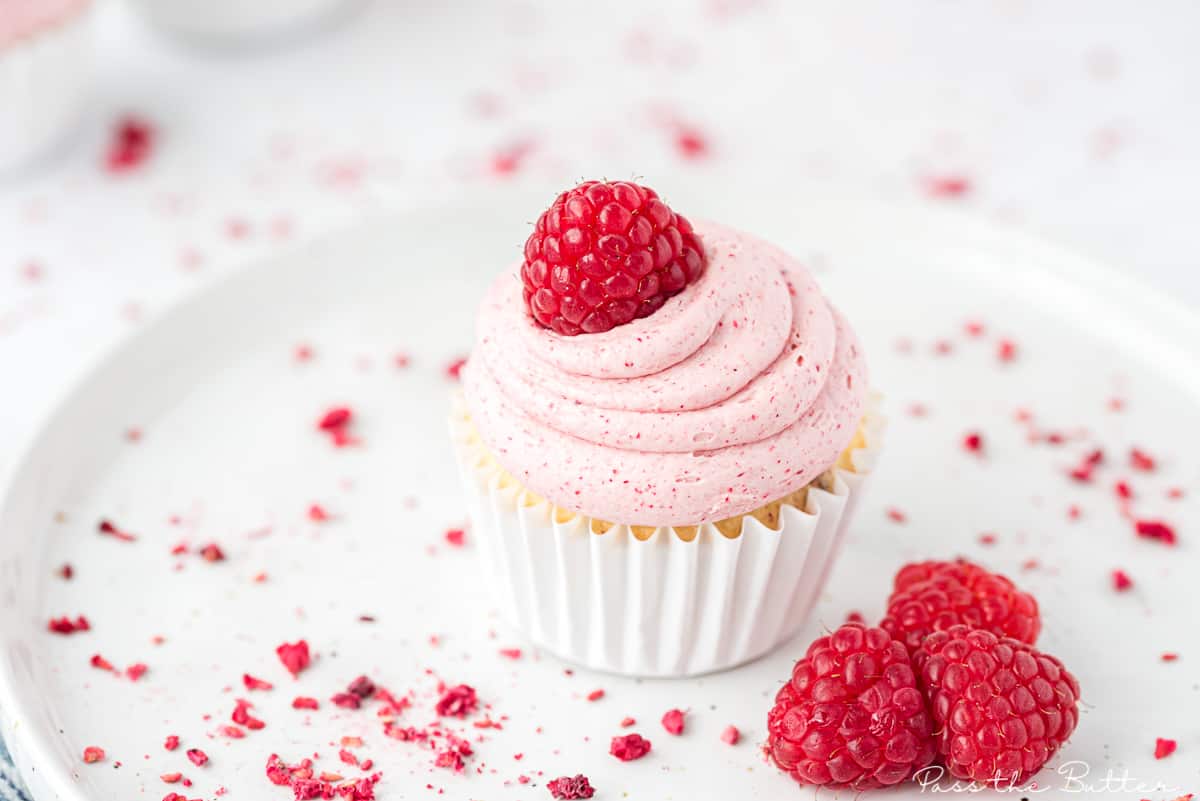 raspberry cupcake on a plate with a garnish of fresh raspberries
