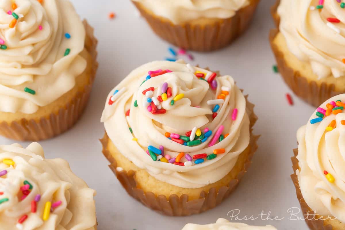 6 vanilla cupcakes with frosting and sprinkles on a plate