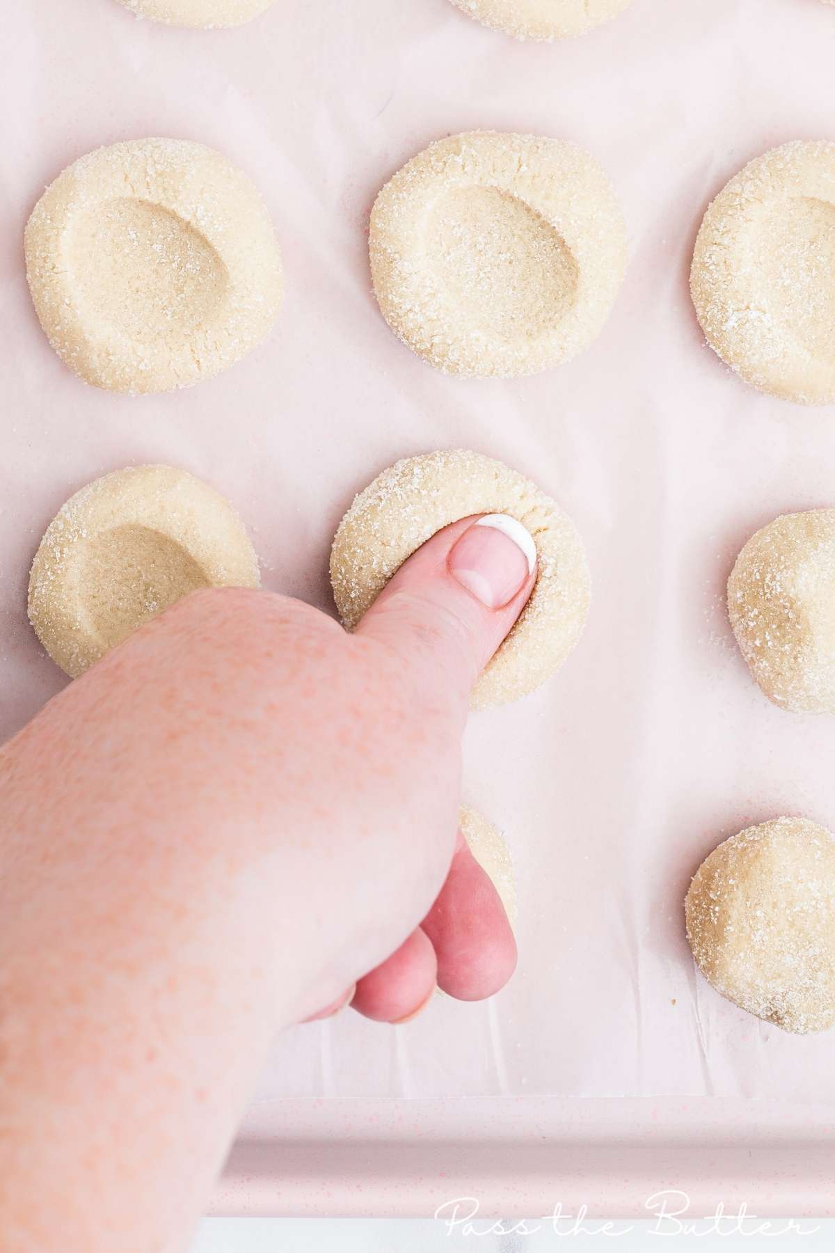 pressing thumb into cookie dough to create thumbprint cookies