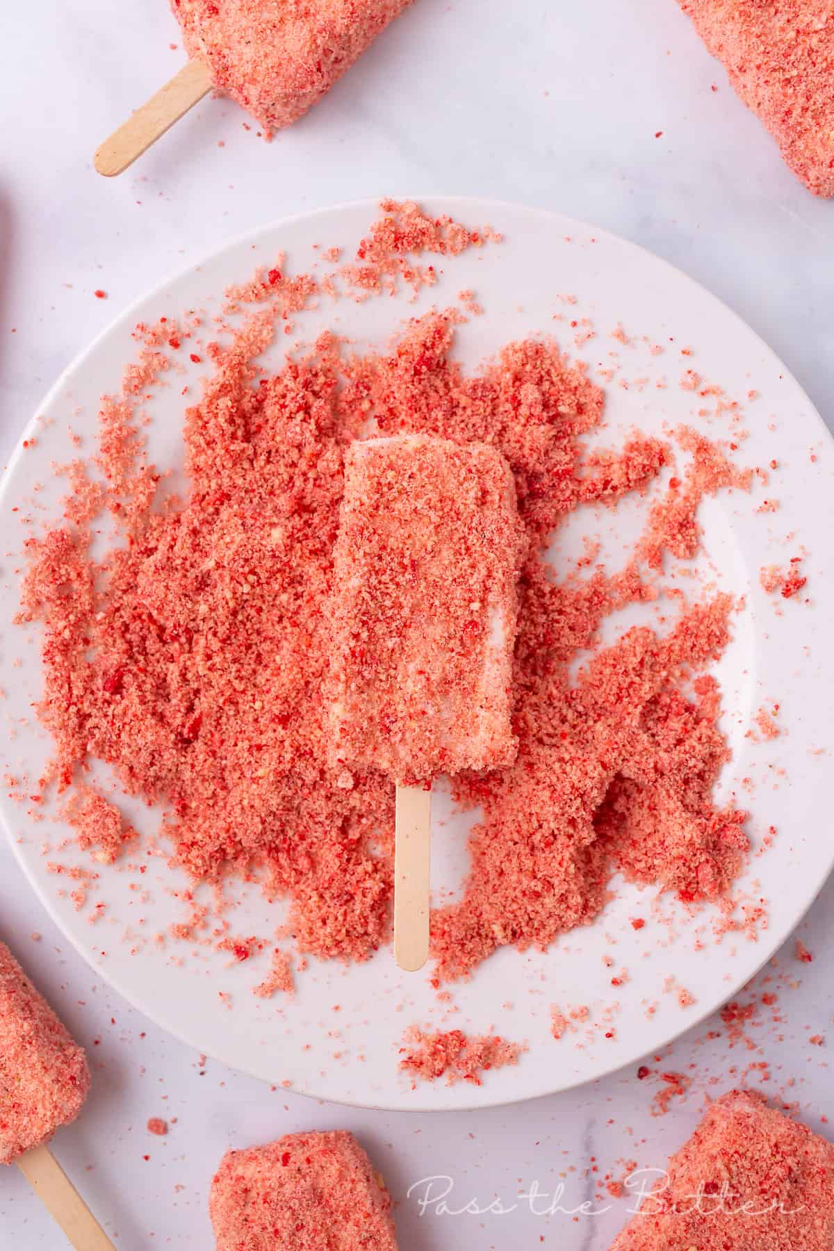 dipping the strawberry shortcake ice cream bar into the strawberry and shortbread coating