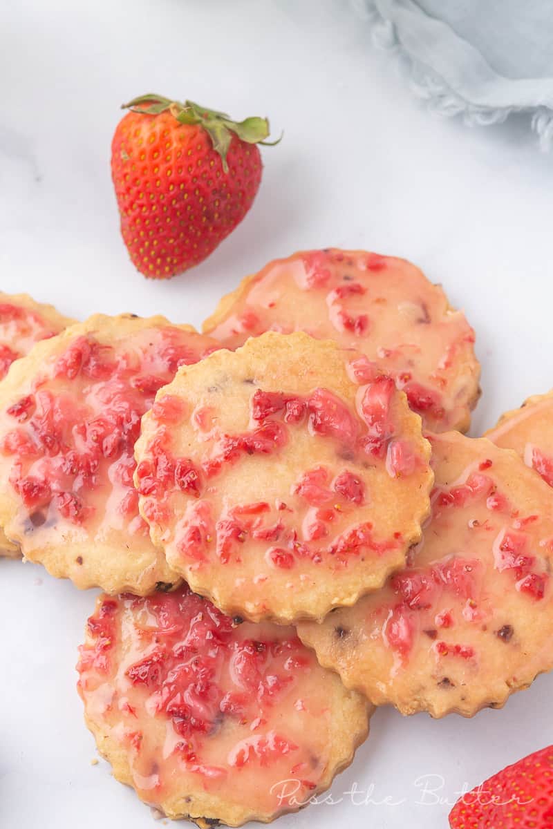 Pile of strawberry shortbread cookies on a marble countertop with fresh strawberries.