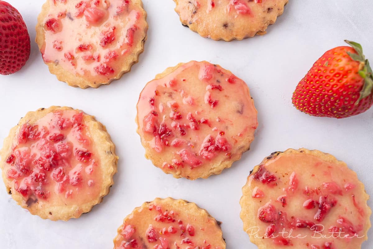Strawberry Shortbread Cookies laid out on a marble counter top with fresh strawberries.